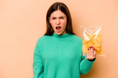 Latin kökenli genç bir kadın elinde bir çanta dolusu cipsle bej arka planda çok sinirli ve agresif çığlıklar atıyor..