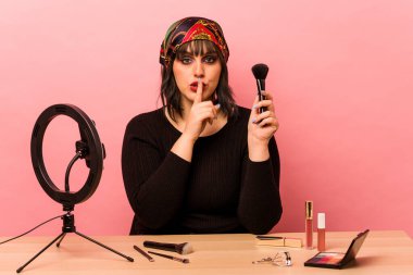 Makyaj sanatçısı genç bir kadın pembe arka planda izole edilmiş bir makyaj dersi veriyor ya sır saklıyor ya da sessizlik istiyor..