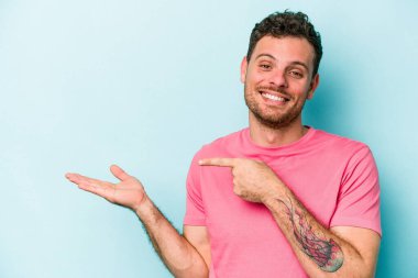 Kafkasyalı genç adam mavi arka planda izole edilmiş. Elinde palmiye ağacının bir kopyası olduğu için heyecanlı..