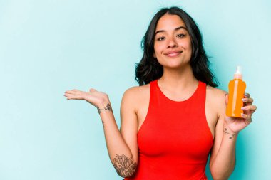 Mavi arka planda izole edilmiş güneş kremi tutan genç İspanyol kadın bir avuç içinde fotokopi alanı ve belinde bir el daha tutuyor..