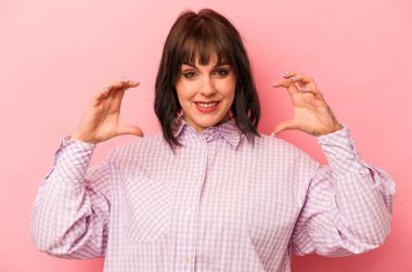 Pembe arka planda izole edilmiş beyaz bir kadın elinde avuç içi bir şeyle kameraya sunuyor..