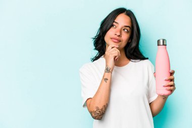 Mavi arka planda termo tutan genç İspanyol kadın şüpheli ve şüpheci bir ifadeyle yana bakıyor..