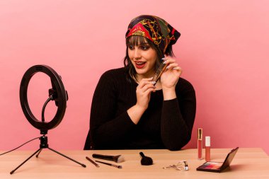 Makyaj sanatçısı genç bir kadın pembe arka planda özel bir makyaj dersi veriyor.