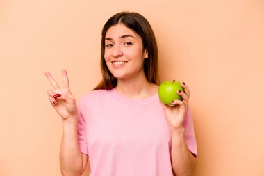 Elma tutan genç İspanyol kadın bej arka planda izole edilmiş iki numarayı parmaklarıyla gösteriyor..