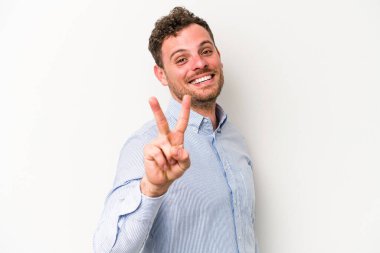 Beyaz arka planda izole edilmiş genç beyaz bir adam zafer işareti gösteriyor ve gülümsüyor..