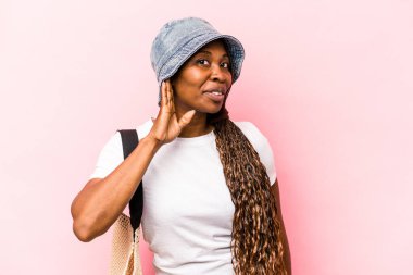 Genç Afrikalı Amerikalı kadın plaja gidiyor. Pembe arka planda izole edilmiş bir şekilde. Dedikoduları dinlemeye çalışıyor..