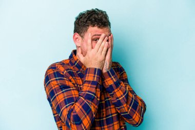 Kafkasyalı genç adam mavi arka planda izole edilmiş. Korkmuş ve gergin parmaklarıyla göz kırp..