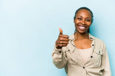 Genç Afrikalı Amerikalı kadın mavi arka planda izole edilmiş gülümsüyor ve başparmağını kaldırıyor.