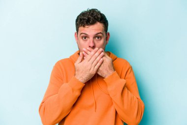 Kafkasyalı genç adam mavi arka planda izole edilmiş ağzı kapalı ve elleri endişeli görünüyor..