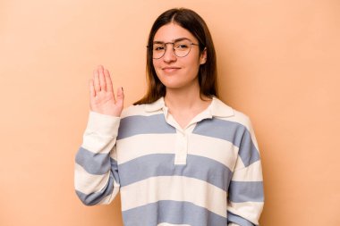 Latin kökenli genç bir kadın bej arka planda izole edilmiş. Gülümsüyor. Beş numarayı parmaklarıyla gösteriyor..