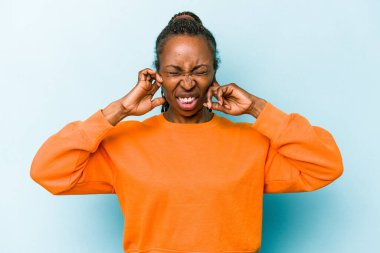 Genç Afrikalı Amerikalı kadın mavi arka planda izole edilmiş kulakları elleriyle kapatıyor..