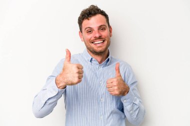Beyaz arka planda izole edilmiş genç beyaz bir adam iki parmağını da kaldırıyor, gülümsüyor ve kendinden emin..