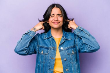 Mor arka planda izole edilmiş, parmaklarıyla kulaklarını kapatan, gürültülü bir ortam tarafından stresli ve çaresiz genç İspanyol kadın..