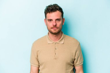 Kafkasyalı genç adam mavi arka planda izole edilmiş üzgün, ciddi yüzlü, mutsuz ve hoşnutsuz..