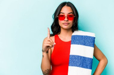Elinde plaj havlusu tutan genç İspanyol kadın mavi arka planda bir numarayı parmağıyla gösteriyor..