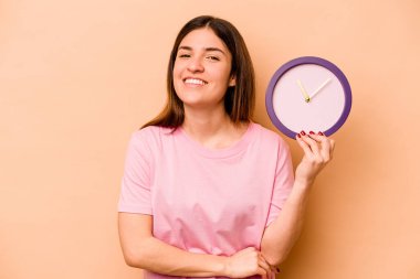 Elinde bej arka planda izole edilmiş bir saat tutan genç İspanyol kadın gülüyor ve eğleniyor..