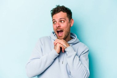 Kafkasyalı genç adam mavi arka planda izole edilmiş şans için dua ediyor, şaşırmış ve ağzını açıp önüne bakıyor..