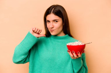 Latin kökenli genç bir kadın bej arka planda izole edilmiş mısır gevreği yiyor gururlu ve kendinden emin hissediyor, örnek olarak..