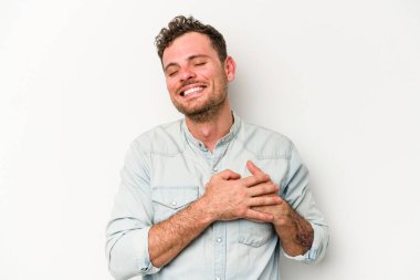 Beyaz arka planda soyutlanmış beyaz tenli genç bir adam gülüyor, elini yüreğine koyuyor, mutluluk kavramını koruyor..
