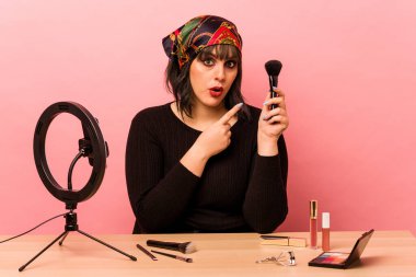 Makyaj eğitmeni genç bir kadın. Pembe arka plana izole edilmiş. Yan tarafı işaret ediyor.