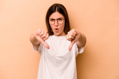 Latin kökenli genç bir kadın bej arka planda izole edilmiş. Baş parmağını aşağı gösteriyor ve hoşlanmadığını ifade ediyor..