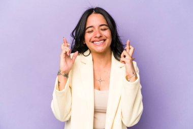 Mor arka planda izole edilmiş genç İspanyol kadın şans dilemek için parmaklarını çapraz yapıyor.