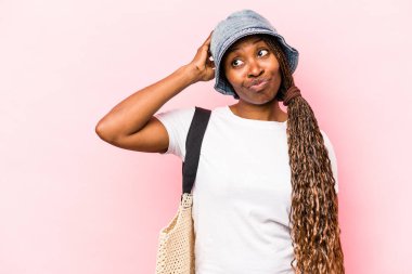 Genç Afrikalı Amerikalı bir kadın pembe arka planda izole bir şekilde kumsala gidiyor. Kafasının arkasına dokunuyor, düşünüyor ve bir seçim yapıyor..