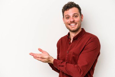 Beyaz arka planda izole edilmiş beyaz tenli genç bir adam palmiyesinde bir kopya alanı tutuyor..