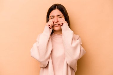 Latin kökenli genç bir kadın, bej arka planda izole edilmiş, sızlanıyor ve ağlıyordu..