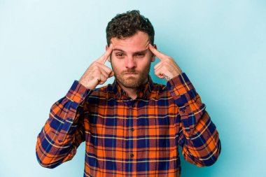 Kafkasyalı genç adam mavi arka planda izole edilmiş bir göreve odaklanmış, parmaklarını işaret ediyor..