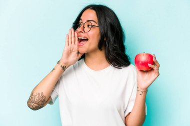 Mavi arka planda izole edilmiş bir elma tutan genç İspanyol kadın bağırıyor ve avuç içini açık tutuyor..