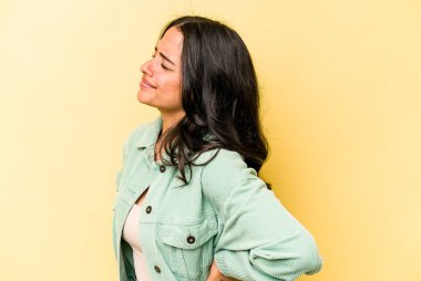 Sarı arka planda izole edilmiş sırt ağrısı çeken genç İspanyol kadın..