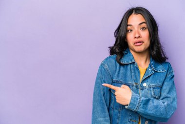 Mor arka planda izole edilmiş genç İspanyol kadın gülümsüyor ve boş alanda bir şeyler gösteriyor..