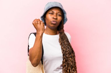 Genç Afrikalı Amerikalı bir kadın pembe arka planda izole bir şekilde kumsala gidiyor. Kameraya yumruğunu gösteriyor, agresif yüz ifadesi..
