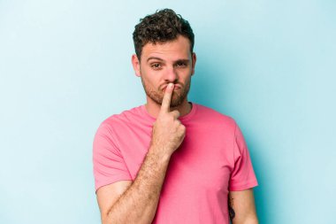 Kafkasyalı genç adam mavi arka planda izole edilmiş düşünüyor ve bakıyor, yansıtıyor, düşünüyor, bir fantezi kuruyor..