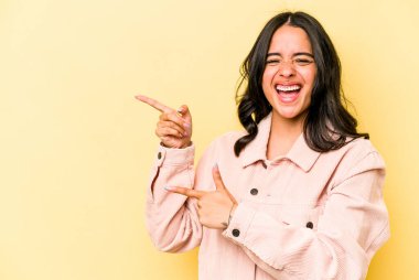 Sarı arka planda izole edilmiş genç İspanyol kadın işaret parmaklarıyla fotokopi alanını işaret ederek heyecan ve arzusunu ifade ediyor..