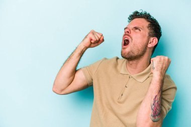 Mavi arka planda izole edilmiş genç beyaz bir adam zaferden sonra yumruğunu kaldırıyor, kazanan konsept..