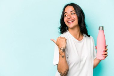 Mavi arka plan noktalarında termo tutan genç İspanyol kadın başparmak uzakta, gülüyor ve kaygısız..