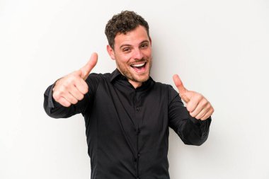 Beyaz arka planda izole edilmiş genç beyaz bir adam iki parmağını da kaldırıyor, gülümsüyor ve kendinden emin..