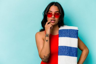 Mavi arka planda izole edilmiş plaj havlusu tutan genç İspanyol kadın rahatlamış fotokopi odasına bakan bir şey düşünüyor..