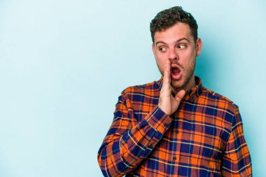 Mavi arka planda izole edilmiş genç beyaz bir adam gizli bir sıcak fren haberi veriyor ve yana bakıyor.