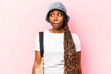 Genç Afrikalı Amerikalı bir kadın pembe arka planda izole edilmiş bir şekilde sahile gidiyor. Kafası karışmış, şüpheli ve kendinden emin değil..