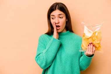 Latin kökenli genç bir kadın, elinde bej arka planda izole edilmiş bir paket cipsle gizli bir sıcak fren haberi veriyor.