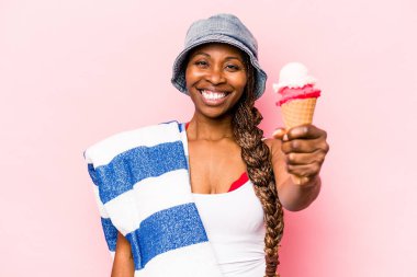 Genç Afrikalı Amerikalı bir kadın plaja gidiyor pembe arka planda izole edilmiş bir dondurma tutuyor.