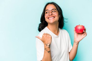 Mavi arka planda bir elma tutan genç İspanyol kadın parmak uzakta, gülüyor ve kaygısız..