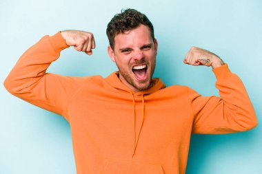 Mavi arka planda izole edilmiş genç beyaz adam güçlü bir hareket sergiliyor kollarıyla, kadınsı gücün sembolü.