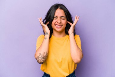 Mor arka planda izole edilmiş genç İspanyol kadın kulaklarını elleriyle kapatıyor..