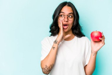 Mavi arka planda izole edilmiş bir elma tutan genç İspanyol kadın gizli bir sıcak fren haberi veriyor ve yana bakıyor.