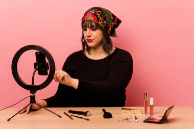 Makyaj sanatçısı genç bir kadın pembe arka planda özel bir makyaj dersi veriyor.