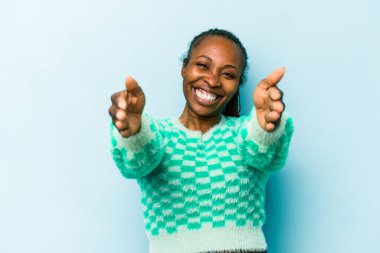 Genç Afrikalı Amerikalı kadın mavi arka planda izole edilmiş zaferi ya da başarıyı kutluyor, şaşırmış ve şok olmuş..